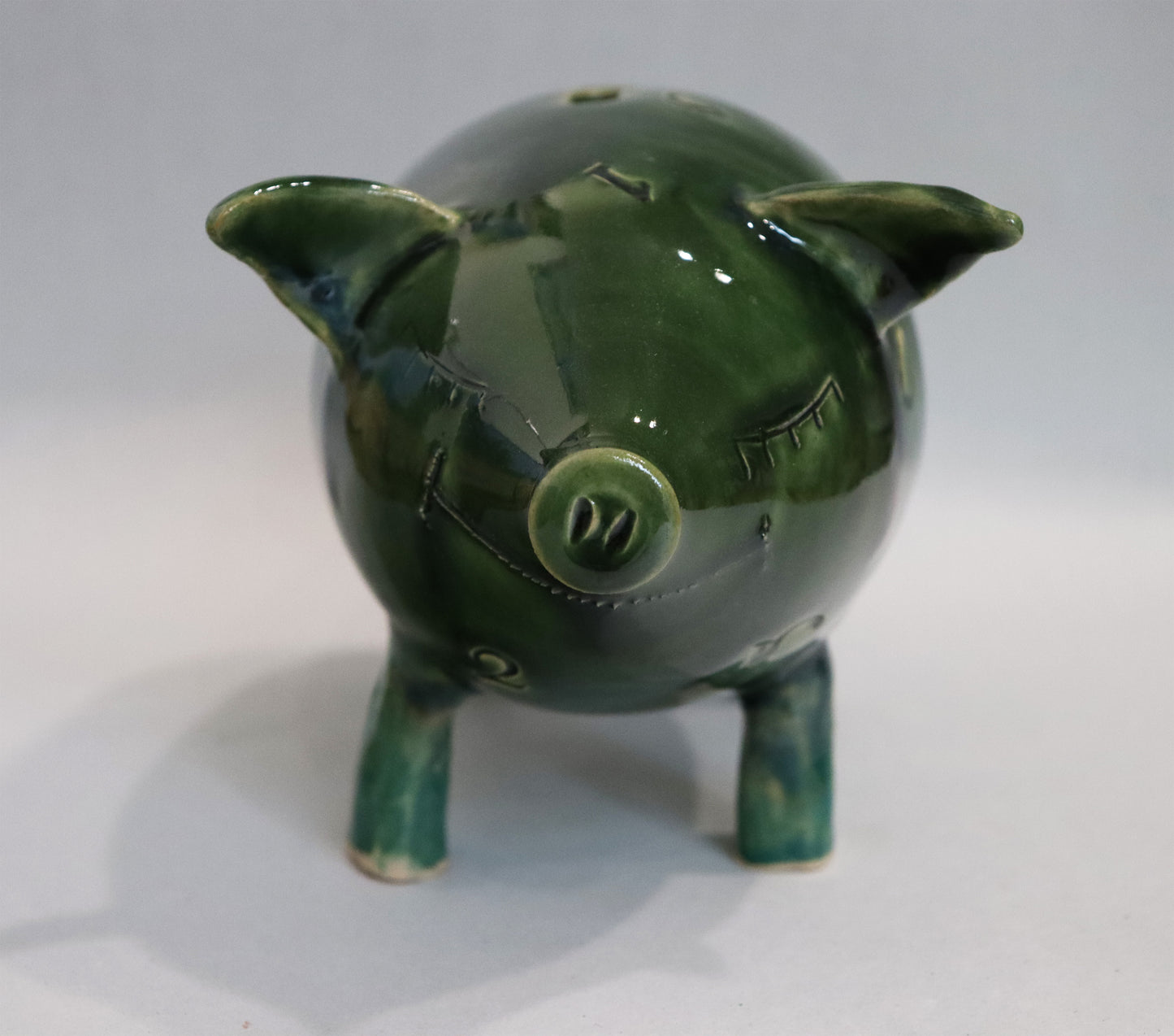 Original Keramik - Sparschwein von Anette Weber, Vorderansicht, Schwein lächelt mit geschlossenen Augen, Farbe grün und türkisgrün, erhältlich bei Galerie Waldbach - What The Artist Made
