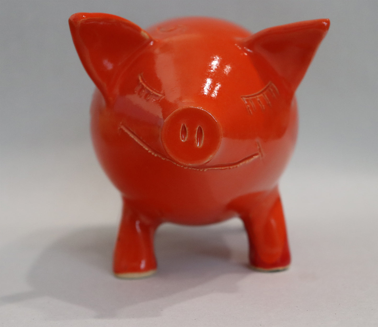 Original Keramik - Sparschwein von Anette Weber, Vorderansicht, Schwein lächelt mit geschlossenen Augen, Farbe rot und orange, erhältlich bei Galerie Waldbach - What The Artist Made