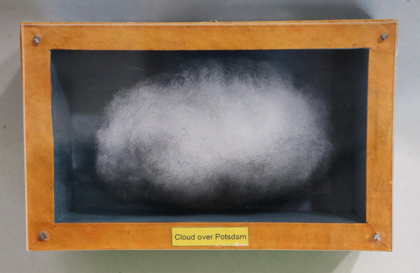 Original Objekt - Assemblage von Elisabeth Dishur, Titel „cloud over Potsdam" – Objektkiste mit Wolke aus Watte, gefärbt. Blauer Hintergrund, Titel unten mittig auf dem Kistenrand. Eingefasst in eine Holzkiste, umseitig Papiercollage mit Stadtkarte, mit Plexiglas versehen - Objektcollage, erhältlich bei Galerie Waldbach - What The Artist Made