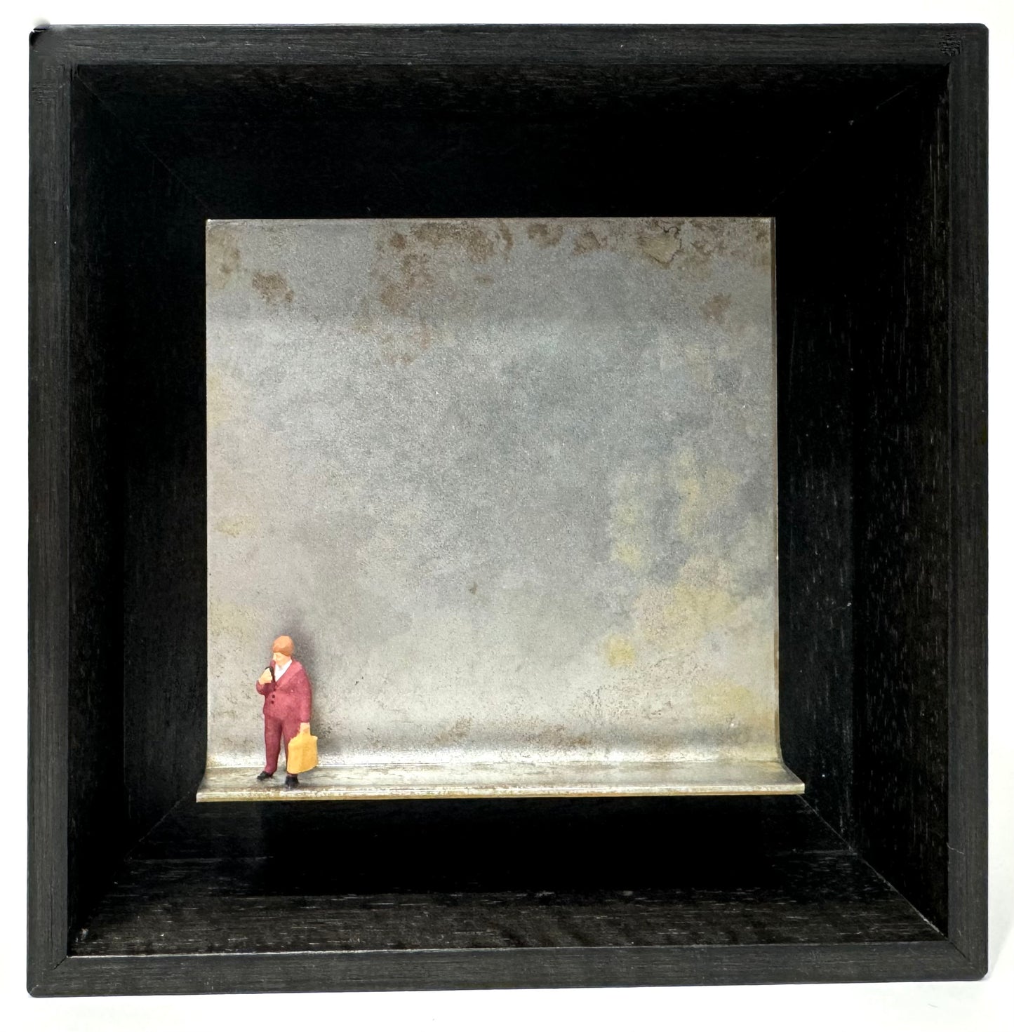 Original Objekt - Assemblage von Katrin Schramm, Titel „geräuschlos regieren…“ – Metallwinkel mit Miniatur-Figur: Frau links am Rand des Winkels stehend, gekleidet in weinroten Hosenanzug, gelbe Arbeitstasche tragend, kurze hellbraune Haare. Dahinter das Metall des Winkels als Hintergrund. - Objektcollage, erhältlich bei What The Artist Made