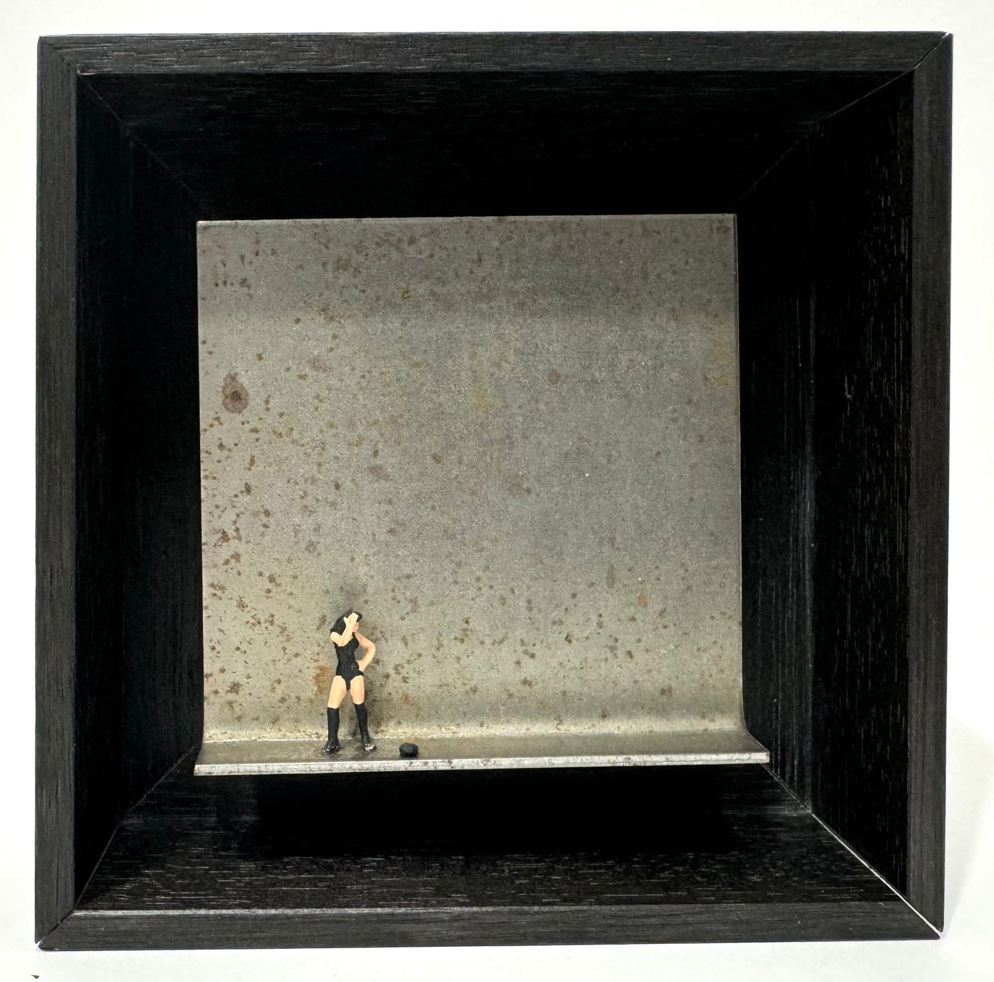 Original Objekt - Assemblage von Katrin Schramm, Titel „nein heißt nein“ – Metallwinkel mit Miniatur-Figur: Frau links am Rand des Winkels stehend, gekleidet in schwarzem Body und Kniestrümpfen. Sie wendet das Gesicht vom Betrachter ab und verdeckt es mit ihrer Hand, die andere Hand in die Hüfte gestemmt. Dahinter das Metall des Winkels als Hintergrund. - Objektcollage, erhältlich bei What The Artist Made