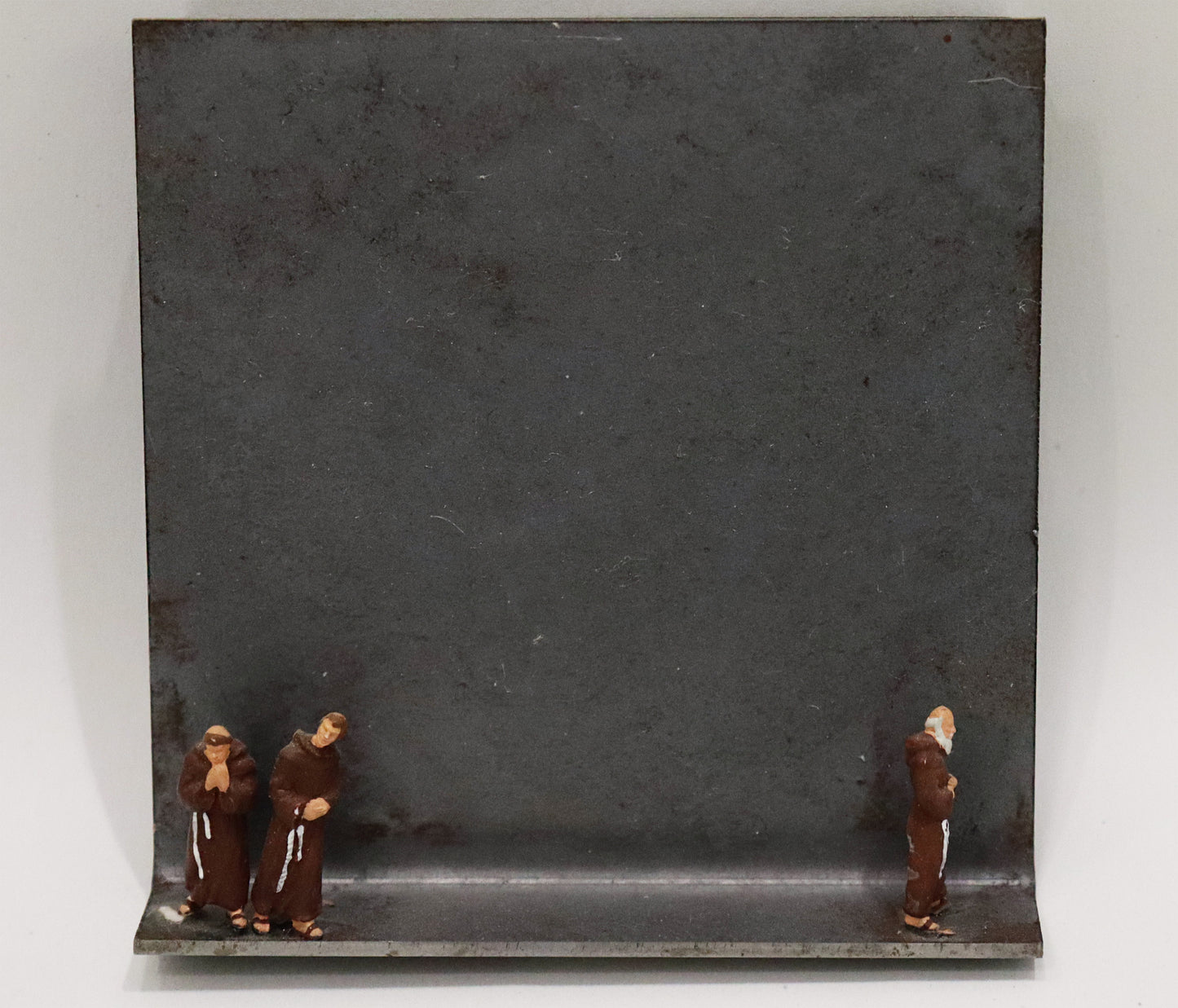 Original Objekt - Assemblage von Katrin Schramm, Titel „vita apostolica“ – Metallwinkel mit Miniatur-Figuren: links am Rand zwei Mönche in braunem Habit stehend, betend, rechts am Rand ein Mönch betend, abgewendet von den beiden anderen stehend. Dahinter das Metall des Winkels mit Struktur, als Hintergrund. - Objektcollage, erhältlich bei Galerie Waldbach - What The Artist Made