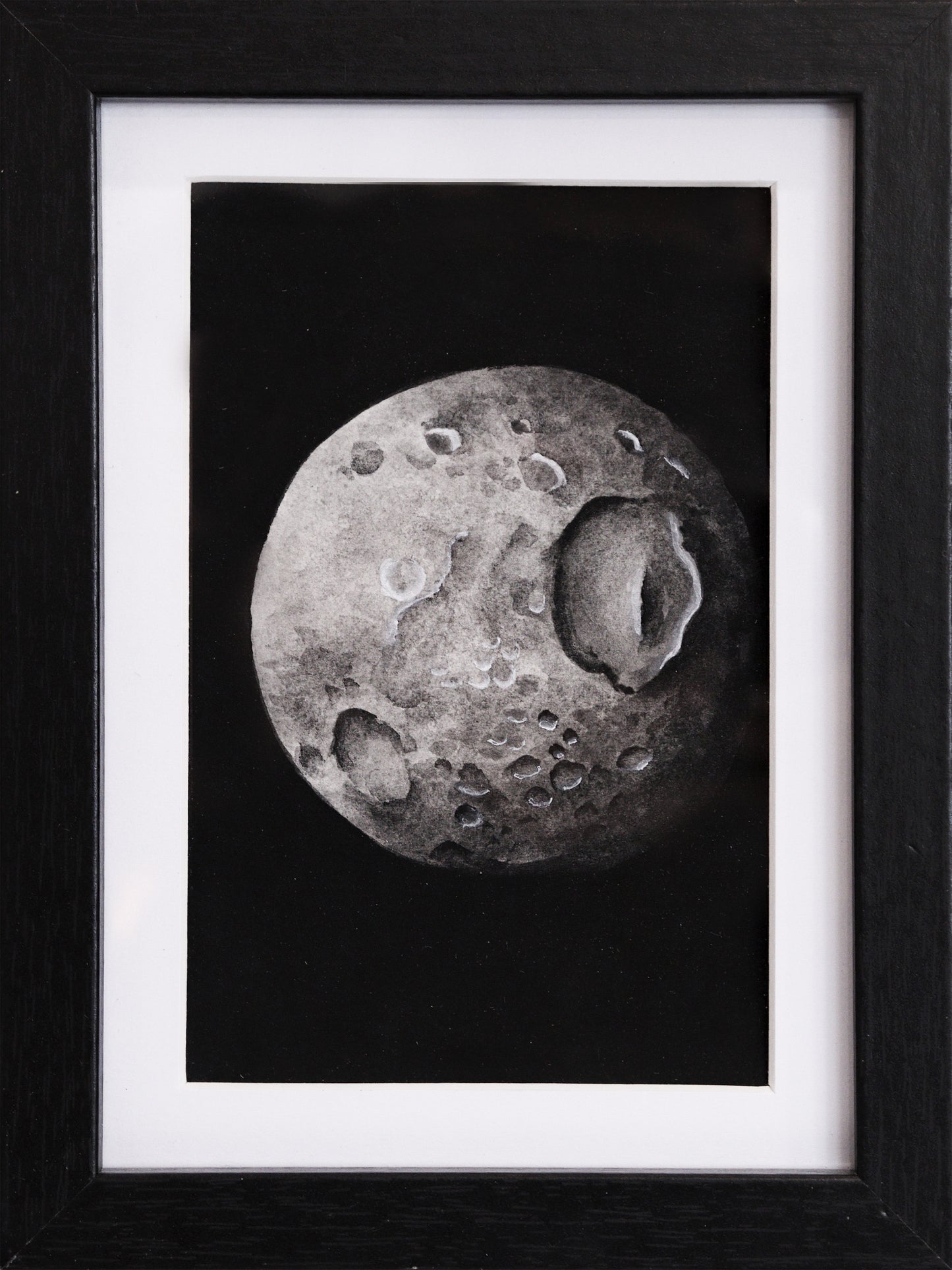 Original Aquarell-Malerei, Gemälde von Lisa Steinbrück, Titel „Mimas“ – Darstellung eines der Monde des Saturns in Aquarell-Stil, schwarz-weiß und Grautöne auf schwarzem Grund, Aquarell auf Papier, gerahmt, schwarzer Rahmen mit weißem Passepartout, erhältlich bei Galerie Waldbach - What The Artist Made