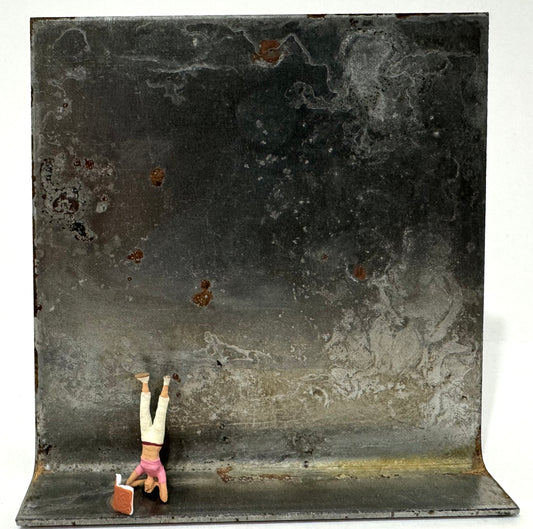 Original Objekt - Assemblage von Katrin Schramm, Titel „ 180°“ – Metallwinkel mit Miniatur-Figur: Frau in Kopfstand links auf dem Winkel stehend, vor ihr ein Buch aufgeklappt stehend. Dahinter das Metall des Winkels als Hintergrund. - Objektcollage, erhältlich bei What The Artist Made