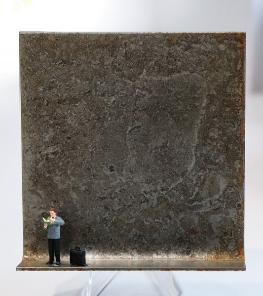 Original Objekt - Assemblage von Katrin Schramm, Titel „Bücher sind Lebensmittel“ – Metallwinkel mit Miniatur-Figur: Ein Mann steht am linken Rand des Winkels und blättert  stehend durch ein Buch, das er hält. Rechts neben ihm steht eine schwarze Aktentasche. Dahinter das Metall des Winkels mit Struktur, als Hintergrund. Objektcollage, erhältlich bei Galerie Waldbach - What The Artist Made