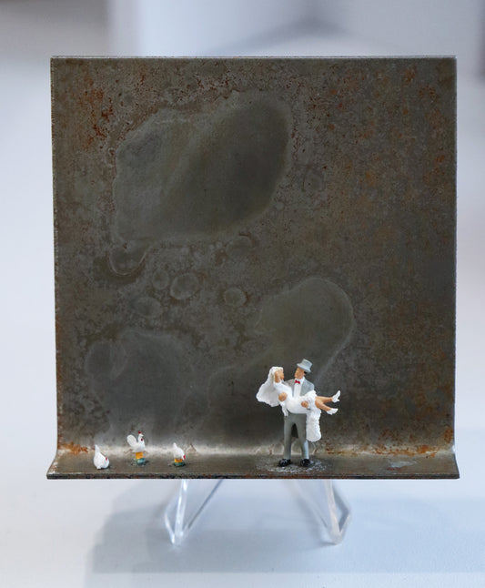 Original Objekt - Assemblage von Katrin Schramm, Titel „Dem Himmel so nah...“ – Metallwinkel mit Miniatur-Figuren: In etwa  der Mitte des Winkels steht ein Bräutigam und trägt die Braut in den Armen. Links neben ihnen am Rand stehen drei weiße Hühner. Dahinter das Metall des Winkels mit Struktur, als Hintergrund. Objektcollage, erhältlich bei Galerie Waldbach - What The Artist Made