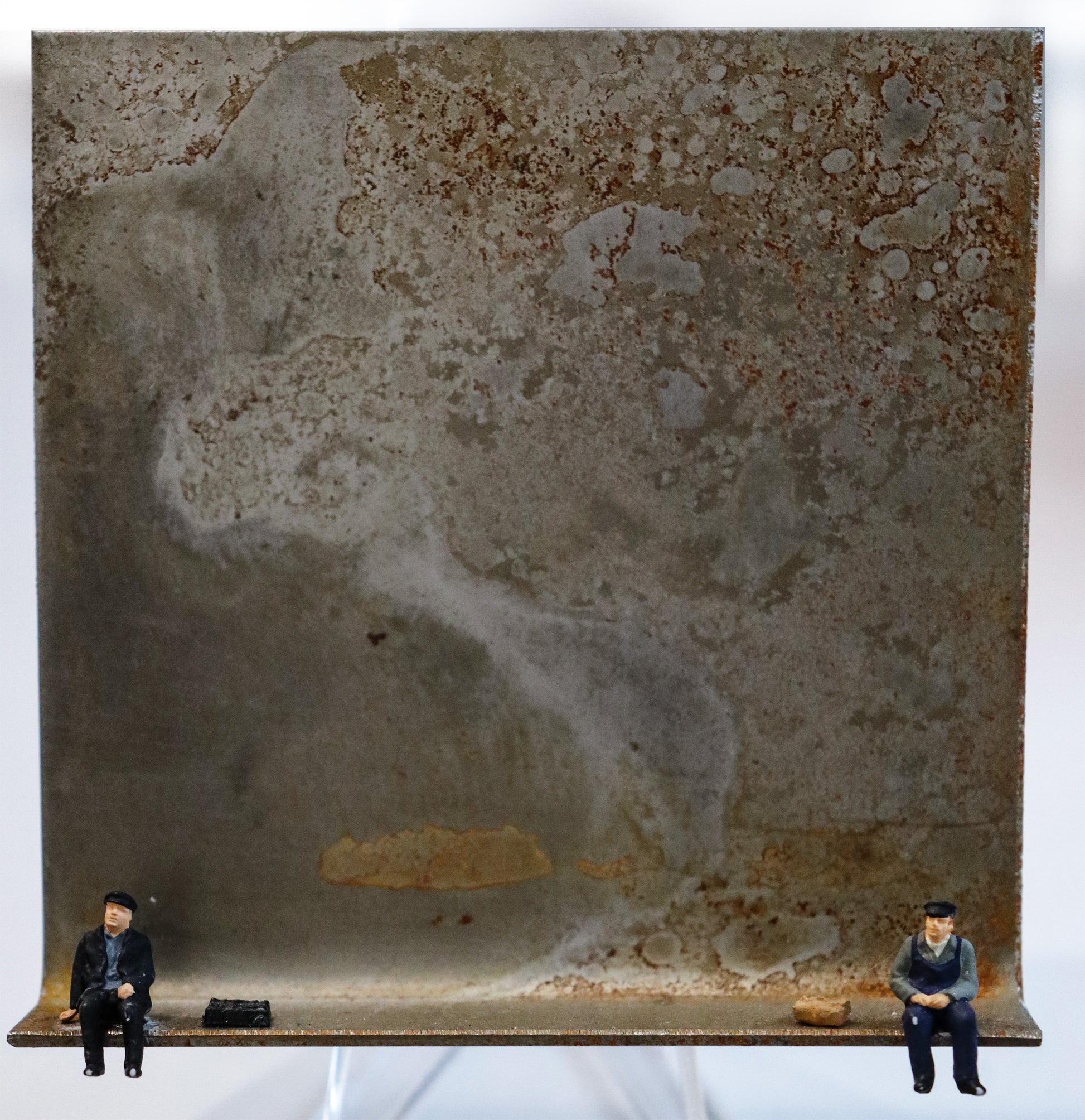 Original Objekt - Assemblage von Katrin Schramm, Titel „ "Moin"   "Moin"  “ – Metallwinkel mit Miniatur-Figuren: Zwei Männer jeweils am Rand des Winkels sitzend, in Arbeiterkleidung. Beide haben ein steinartiges Objekt neben sich liegen. Dahinter das Metall des Winkels mit Struktur, als Hintergrund. - Objektcollage, erhältlich bei Galerie Waldbach - What The Artist Made