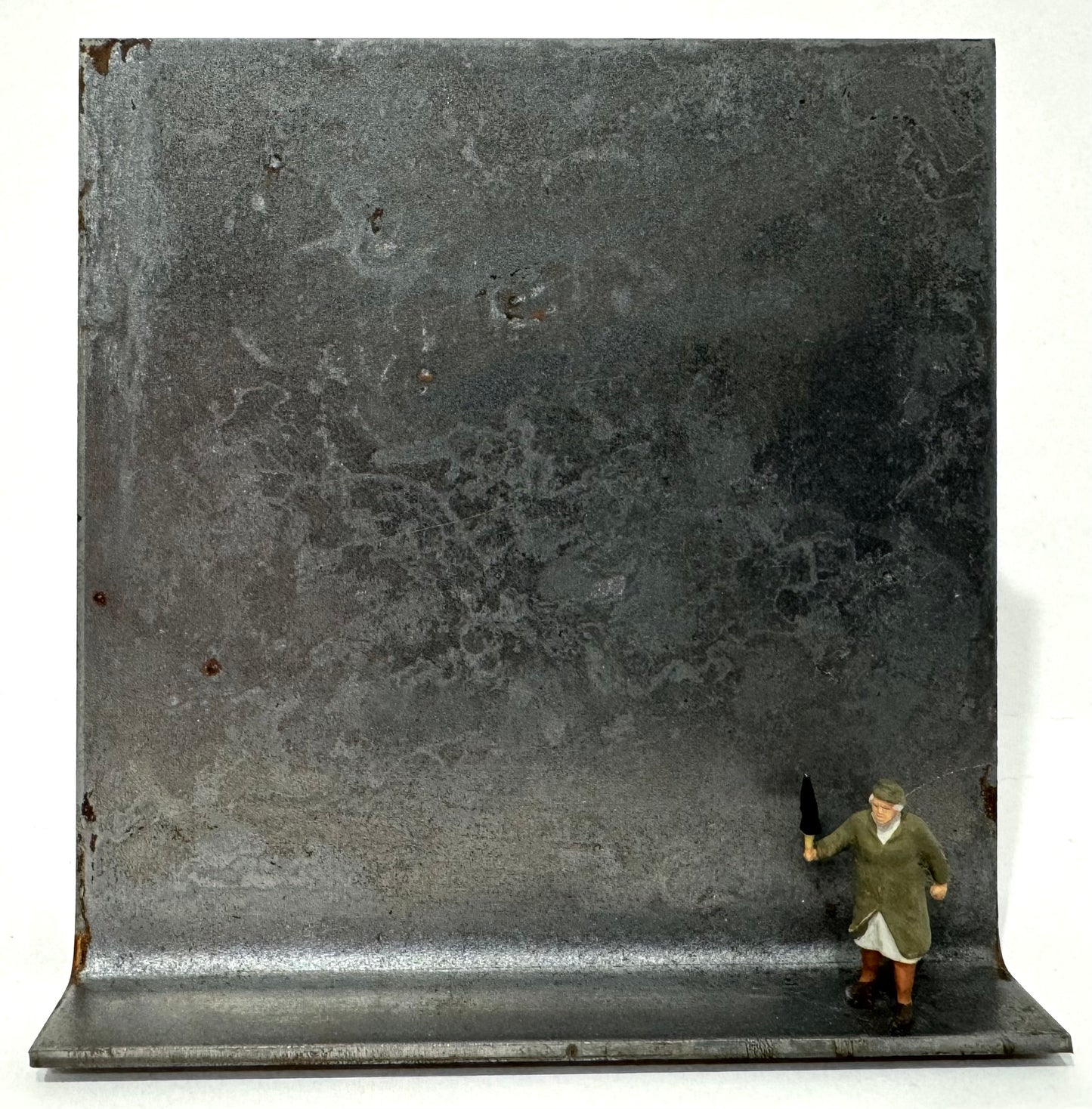 Original Objekt - Assemblage von Katrin Schramm, Titel „Na warte, Bürschchen“ – Metallwinkel mit Miniatur-Figur: ältere Frau rechts auf dem Winkel stehend - sie hält drohend den geschlossenen Regenschirm hoch. Dahinter das Metall des Winkels als Hintergrund. - Objektcollage, erhältlich bei What The Artist Made