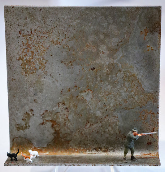 Original Objekt - Assemblage von Katrin Schramm, Titel „Wer mit Katzen auf Jagd geht...“ – Metallwinkel mit Miniatur-Figuren:  Ein Jäger mit Gewehr am rechten Rand stehend, das Gewehr auf einen Punkt außerhalb des Winkels ausgerichtet. Am linken Bildrand drei Katzen, eine schwarze, eine mit rot-weißem Fell und eine ganz in weiß. Dahinter das Metall des Winkels mit Struktur, als Hintergrund. - Objektcollage, erhältlich bei Galerie Waldbach - What The Artist Made