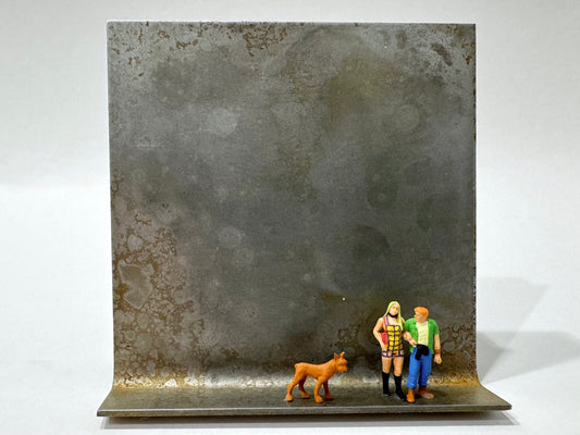 Original Objekt - Assemblage von Katrin Schramm, Titel „Wir sind jetzt zu dritt“ – Metallwinkel mit Miniatur-Figuren: ein Paar auf dem Winkel stehend, neben beiden ein brauner Hund, dahinter das Metall des Winkels als Hintergrund. - Objektcollage, erhältlich bei What The Artist Made