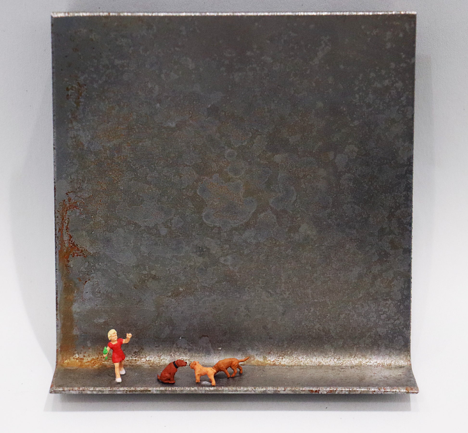Original Objekt - Assemblage von Katrin Schramm, Titel „Wir wollen nur spielen...“ – Metallwinkel mit Miniatur-Figuren: ein Kind/Mädchen mit rotem Kleid, rechts daneben Gruppe aus drei Hunden sitzend/stehend. Dahinter das Metall des Winkels mit Struktur, als Hintergrund. - Objektcollage, erhältlich bei Galerie Waldbach - What The Artist Made
