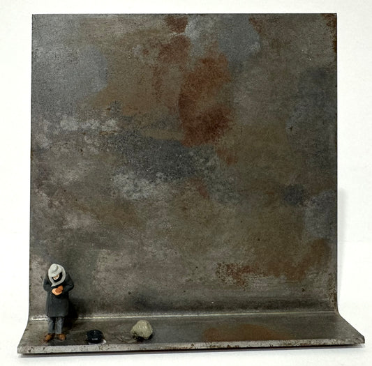 Original Objekt - Assemblage von Katrin Schramm, Titel „geben…“ – Metallwinkel mit Miniatur-Figur: Person am linken Rand des Metallwinkels stehend, Kopf gebeugt, etwas in der Hand haltend. Neben dem Mann ein Gefäß liegend, evtl. ein Hut, daneben ein größerer Stein/Fels. Dahinter das Metall des Winkels als Hintergrund. - Objektcollage, erhältlich bei What The Artist Made