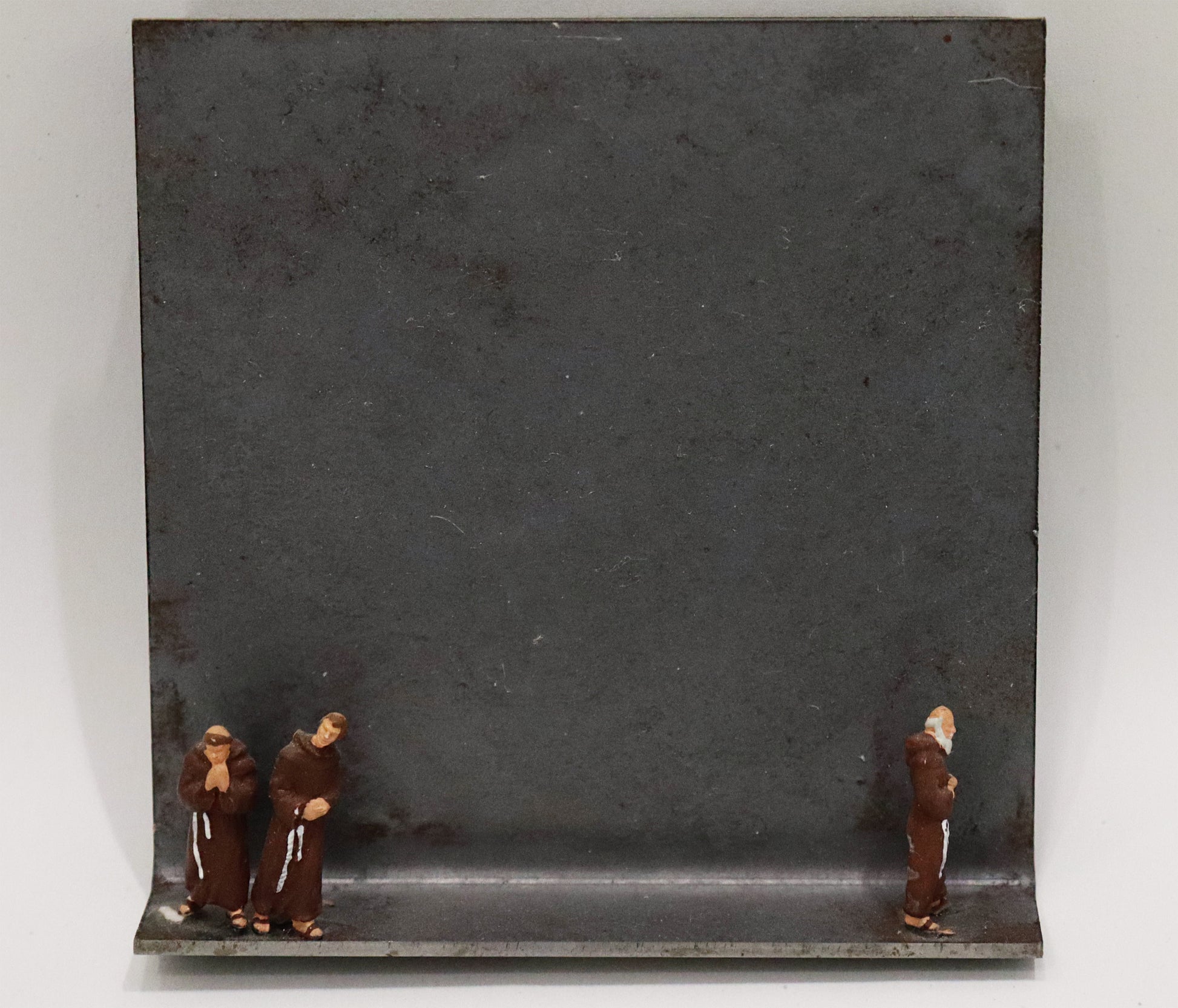 Original Objekt - Assemblage von Katrin Schramm, Titel „vita apostolica“ – Metallwinkel mit Miniatur-Figuren: links am Rand zwei Mönche in braunem Habit stehend, betend, rechts am Rand ein Mönch betend, abgewendet von den beiden anderen stehend. Dahinter das Metall des Winkels mit Struktur, als Hintergrund. - Objektcollage, erhältlich bei Galerie Waldbach - What The Artist Made