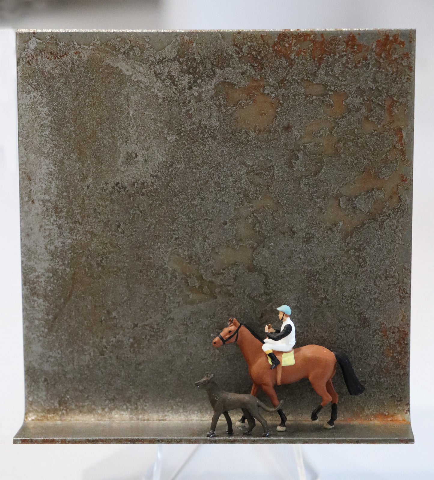 Original Objekt - Assemblage von Katrin Schramm, Titel „Never walk alone...“ – Metallwinkel mit Miniatur-Figuren: Ein Reiter, auf seinem braunen Pferd sitzend läuft von rechts nach links zur Mitte des Winkels, vor ihm ein großer  grauer Hund. Dahinter das Metall des Winkels mit Struktur, als Hintergrund. Objektcollage, erhältlich bei Galerie Waldbach - What The Artist Made