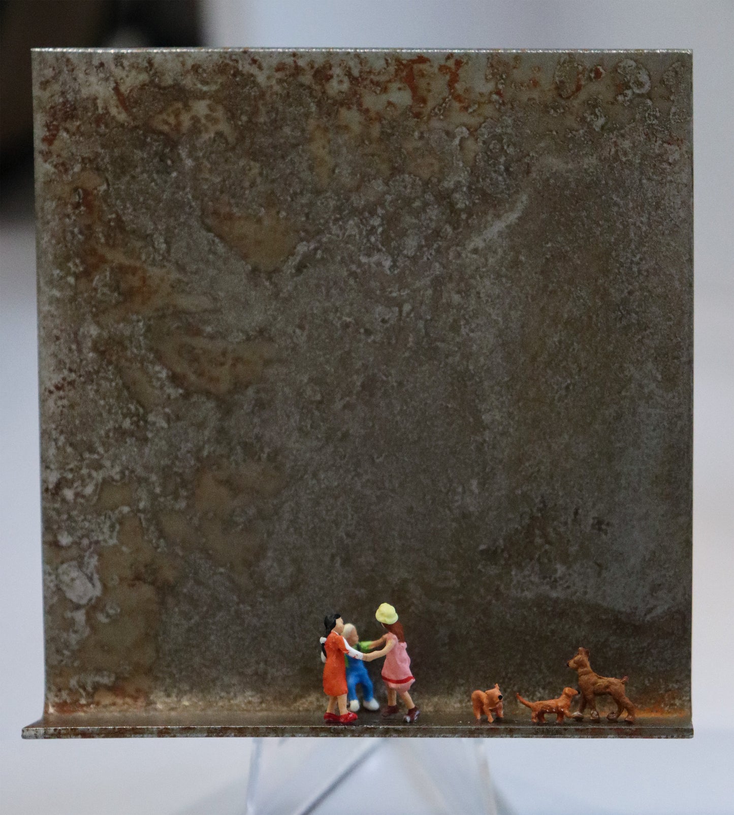 Original Objekt - Assemblage von Katrin Schramm, Titel „Wir wollen nur spielen...“ – Metallwinkel mit Miniatur-Figuren: Drei Kinder tanzen mittig auf dem Rahmen im Ringelreigen, im Kreis. Rechts neben ihnen sind drei braune Hunde, die ihre Formation nachbilden. Dahinter das Metall des Winkels mit Struktur, als Hintergrund. Objektcollage, erhältlich bei Galerie Waldbach - What The Artist Made