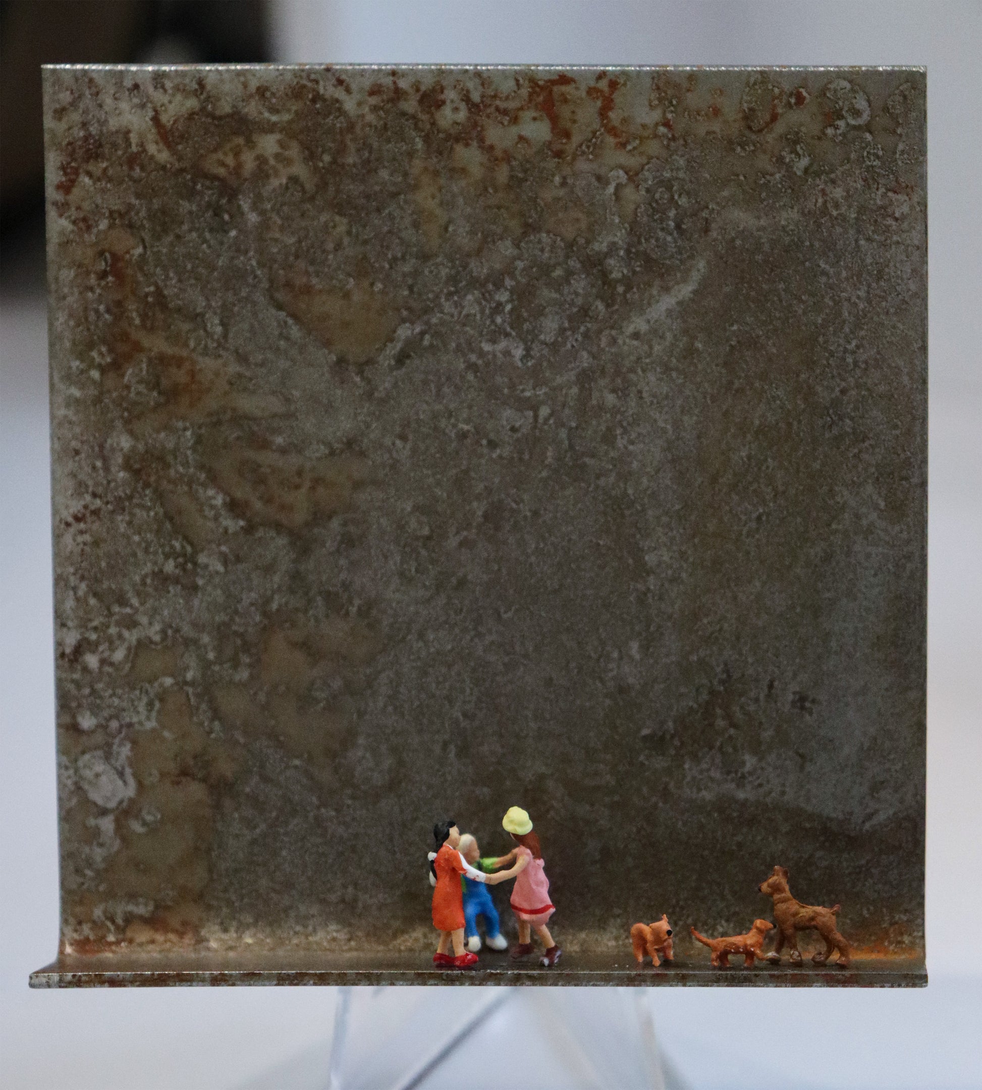 Original Objekt - Assemblage von Katrin Schramm, Titel „Wir wollen nur spielen...“ – Metallwinkel mit Miniatur-Figuren: Drei Kinder tanzen mittig auf dem Rahmen im Ringelreigen, im Kreis. Rechts neben ihnen sind drei braune Hunde, die ihre Formation nachbilden. Dahinter das Metall des Winkels mit Struktur, als Hintergrund. Objektcollage, erhältlich bei Galerie Waldbach - What The Artist Made
